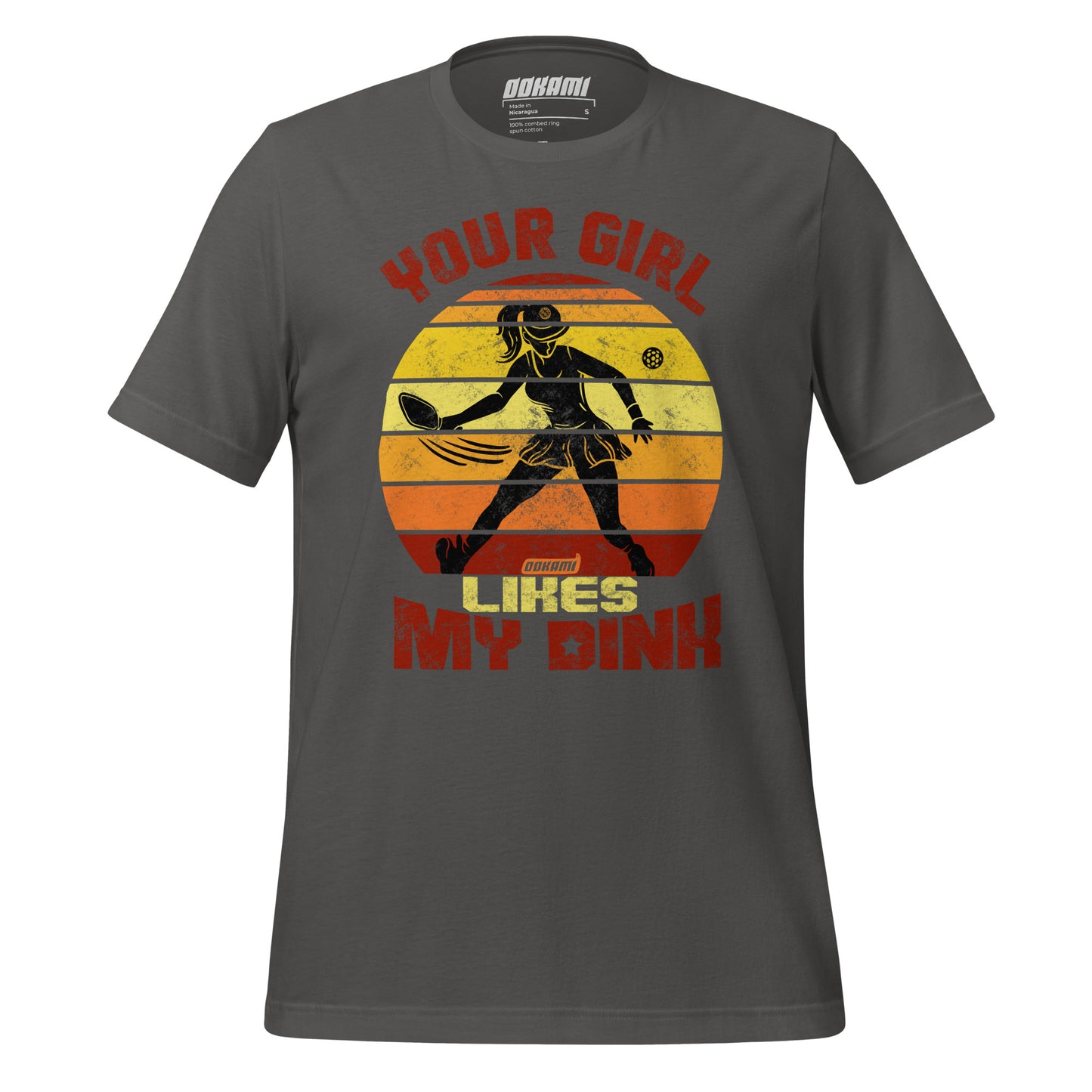 Front view of an asphalt gray unisex t-shirt with a humorous pickleball design. The graphic displays a retro sunset backdrop with a silhouette of a pickleball player and the text 'Your Girl Likes My Dink' in bold distressed fonts. Made with high-quality fabric for pickleball lovers. Available exclusively at Ookami Sports.