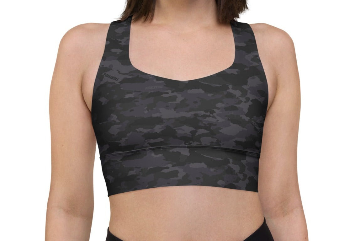 Front view of a woman wearing the Stealth Camo Pickleball Longline Sports Bra, featuring a dark camouflage pattern, high neckline, and wide shoulder straps.