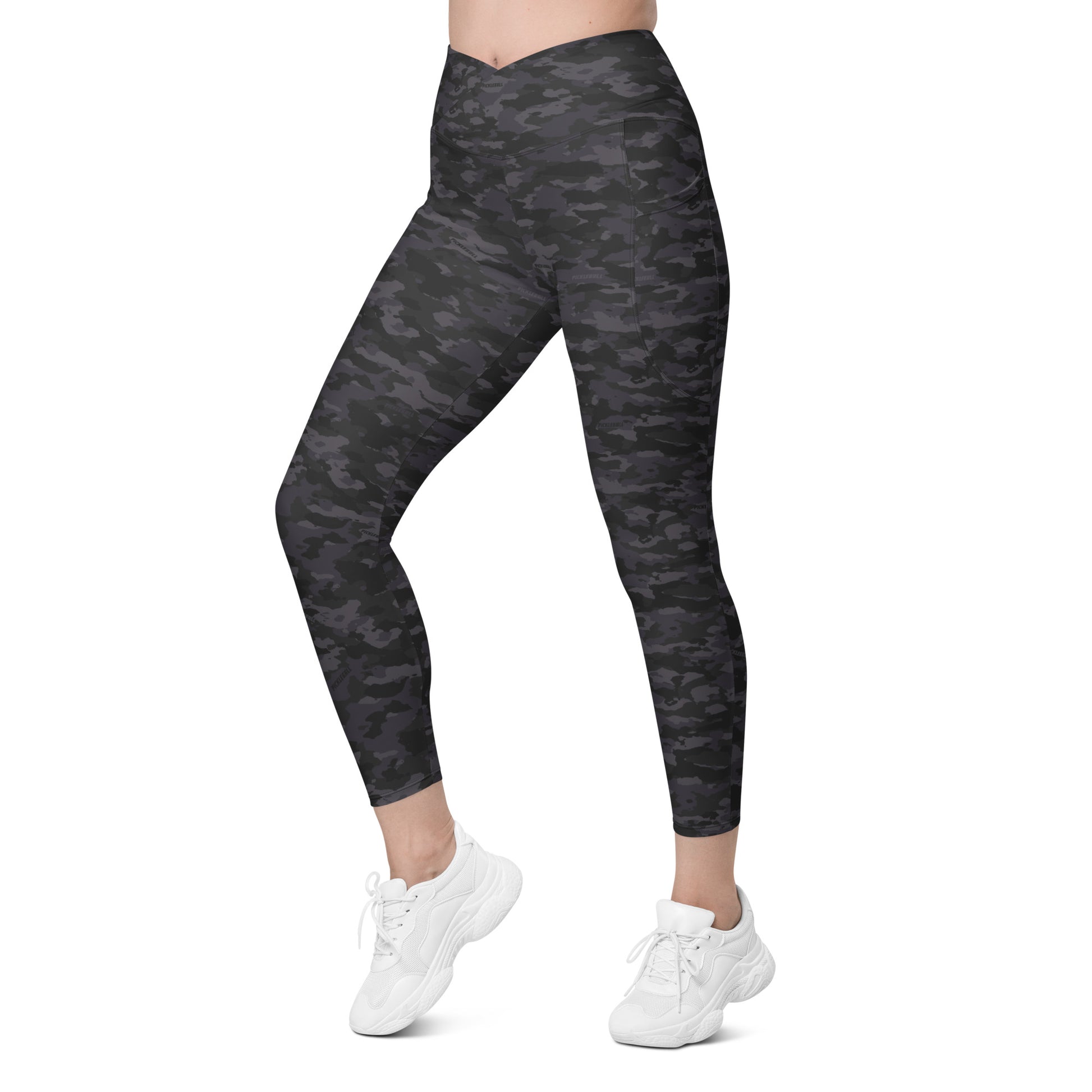 Woman wearing Stealth Camo Pickleball High-Waisted Crossover Leggings in a dark camouflage pattern, showing a left side view with a high-waisted, V-shaped crossover waistband and ankle-length fit.