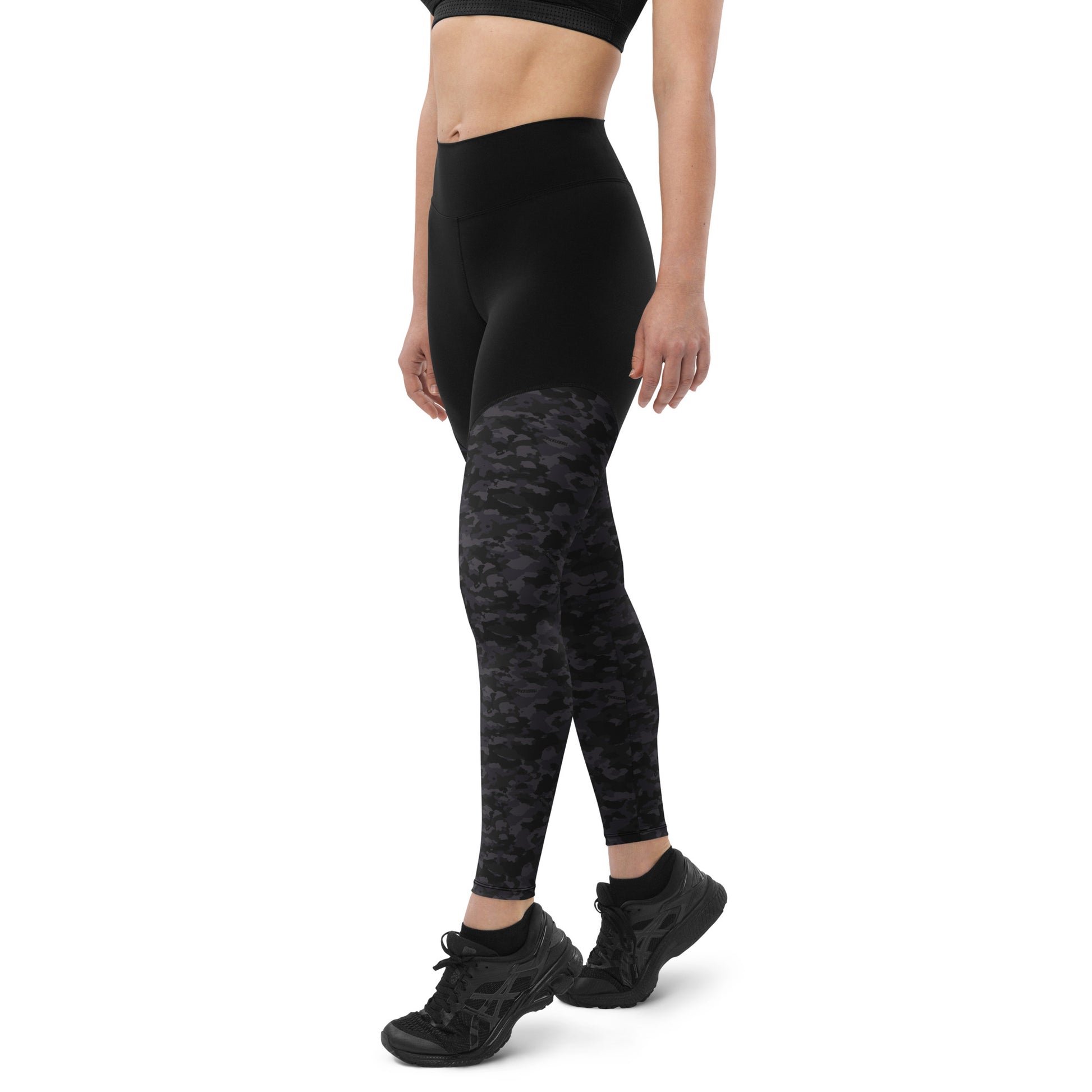 Side view of a woman wearing Stealth Camo Pickleball Sports Leggings, showing the high-waisted design, black upper section, and dark camouflage print on the lower leg.