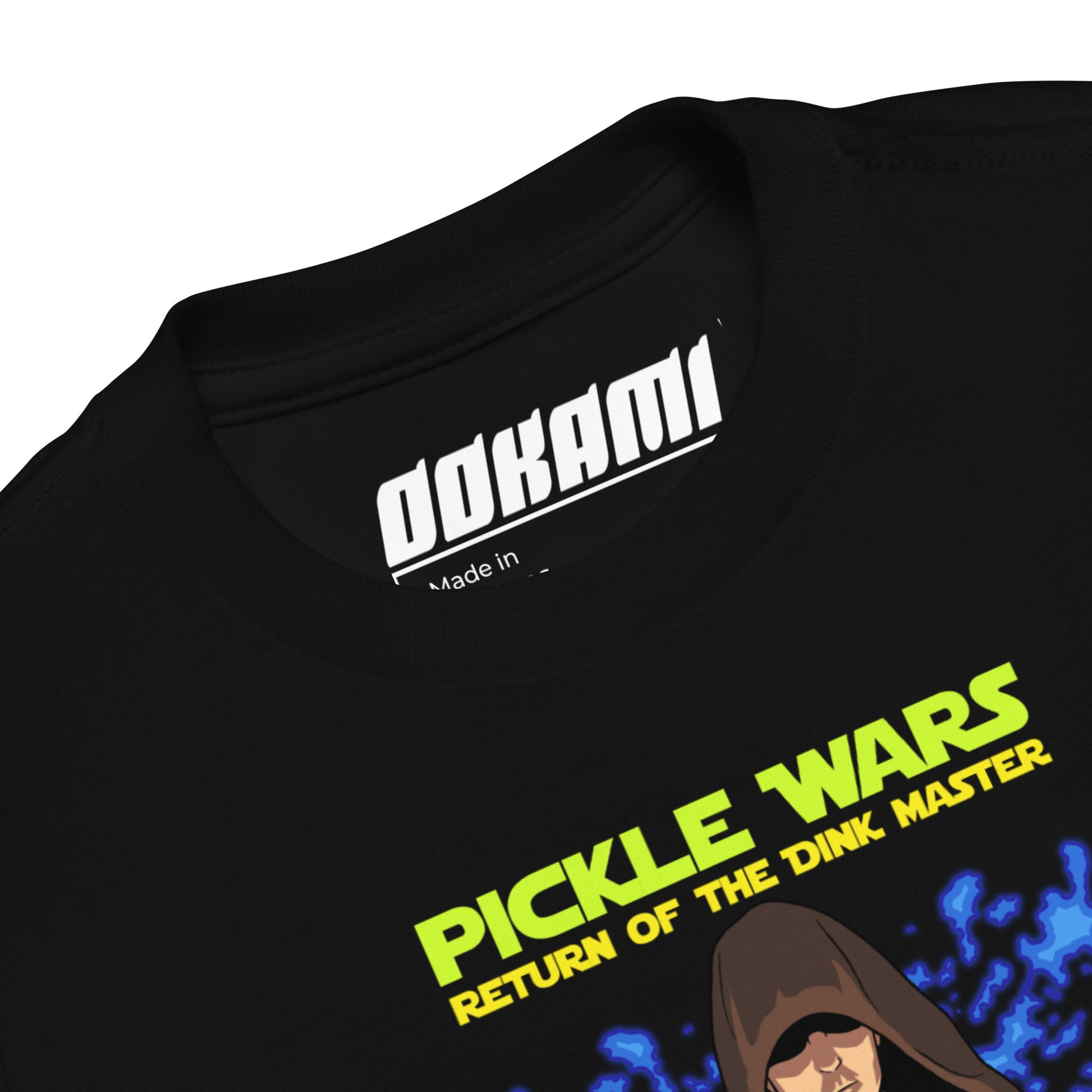 Close-up view of the neckline of the black "Pickle Wars" toddler t-shirt showing the "Ookami" label.