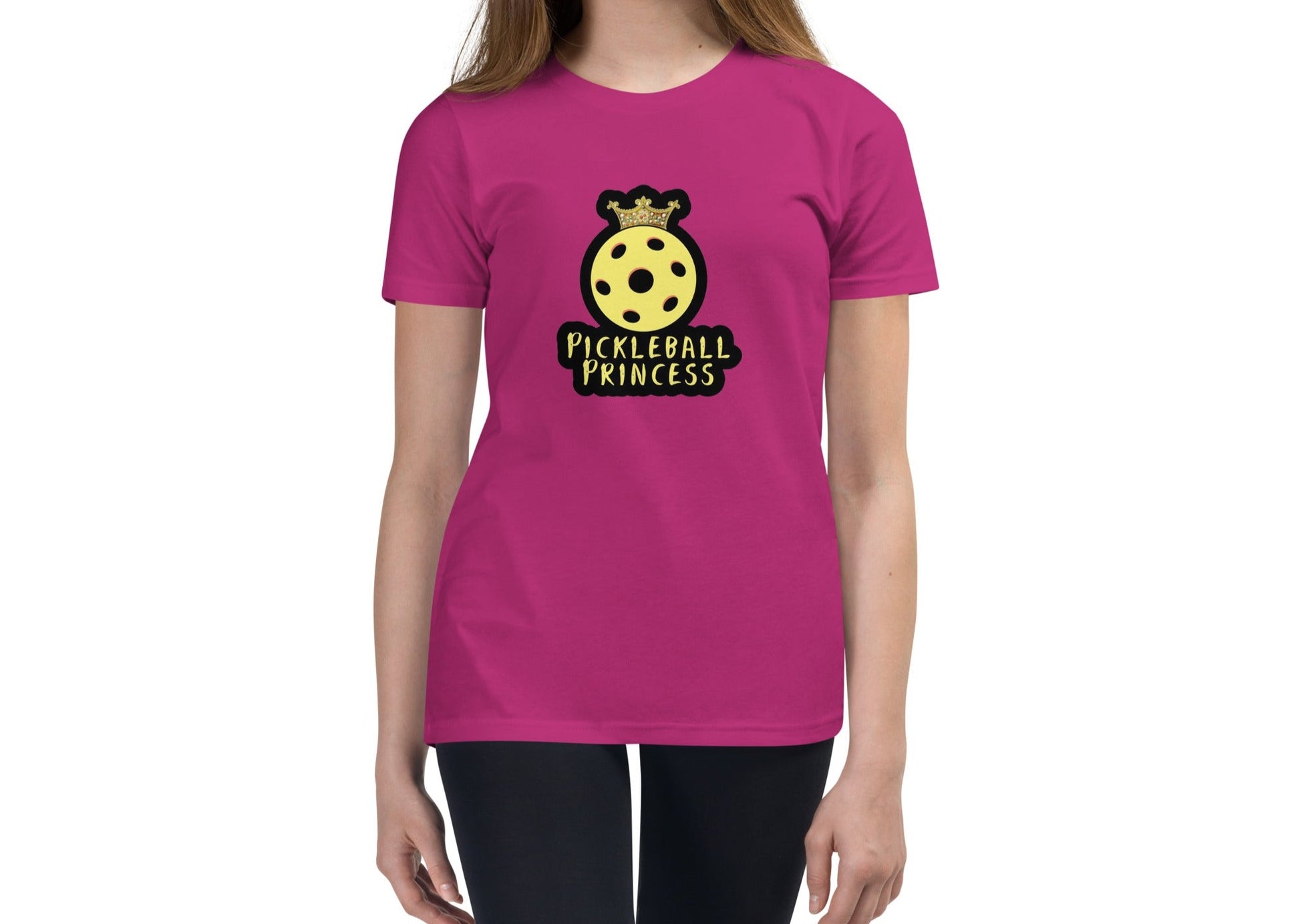 Front view of a pink youth t-shirt worn by a model, featuring a yellow pickleball with a crown and the text "Pickleball Princess.